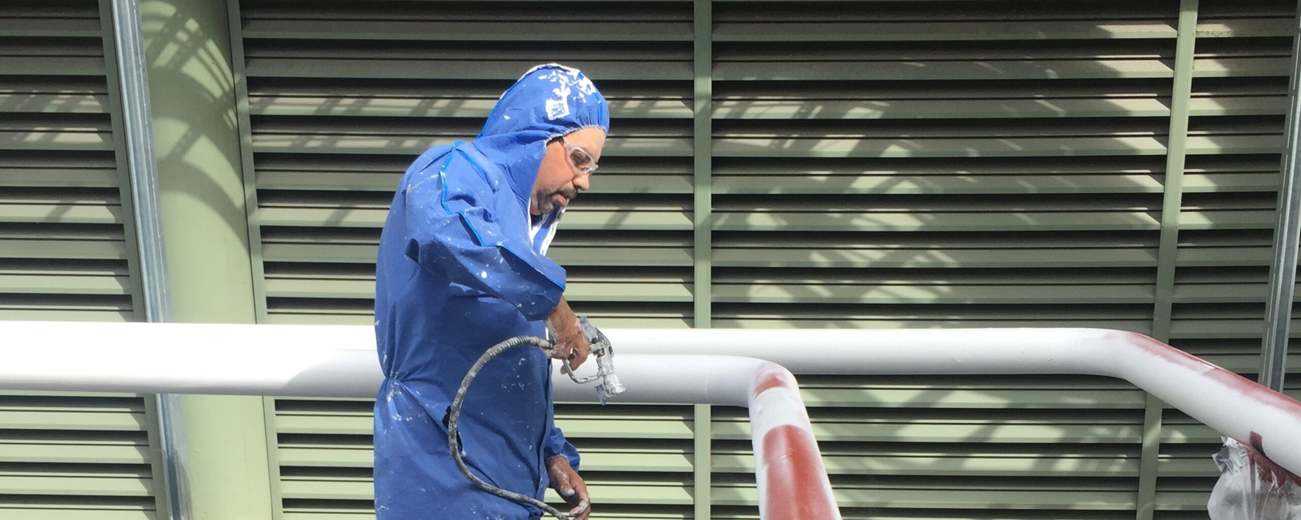 Worker in blue protective suit applying industrial coating to metal piping system